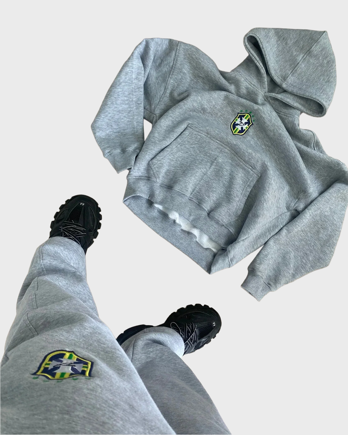 Grey BRASIL pullover hoodie and matching joggers with crest details, styled with black trainers